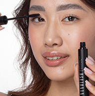 Man sieht eine Frau, die Mascara auf ihre Augen aufträgt und den Pinsel vorsichtig hält, während sie ihre Wimpern betont.