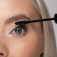 Eine Frau trägt Mascara mit einer Mascara-Bürste auf und betont so gekonnt ihre Wimpern für ein dramatischeres Erscheinungsbild.