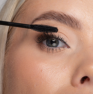 Eine Frau trägt mit einer Mascara-Bürste vorsichtig Mascara auf ihre Wimpern auf und verbessert so ihr Augen-Make-up präzise.