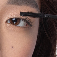 Eine Frau trägt Mascara mit einem Pinsel auf und konzentriert sich dabei auf ihre Wimpern, um einen definierten und eleganten Look zu erzielen.